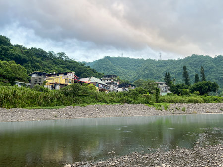 Colorful riverside houses nestled on a hill above the stream in Wulai, New Taipei City, Taiwan. Lush green subtropical mountains frame the quiet, overcast morning scene.の写真素材