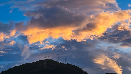 Stunning sky over Wulai New Taipei City Taiwan at dawn or dusk. Dramatic orange and gray clouds hover above power transmission towers on a forested mountain.の写真素材