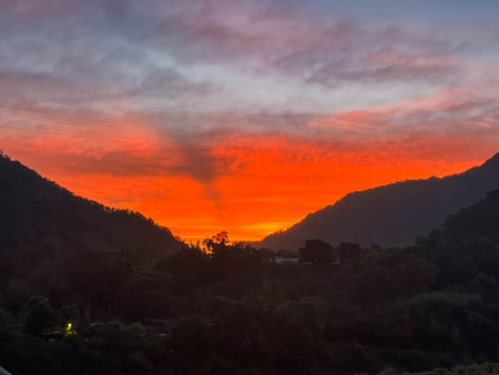Intense fiery orange and red sunrise illuminating dramatic clouds above the dark silhouetted mountains of Wulai, New Taipei City, Taiwan.の写真素材