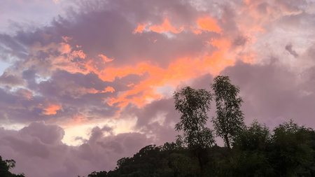 Dramatic dawn sky over Wulai, New Taipei City, Taiwan, featuring vibrant pink, orange, and purple altocumulus clouds above the dark silhouette of the hills and trees.の写真素材