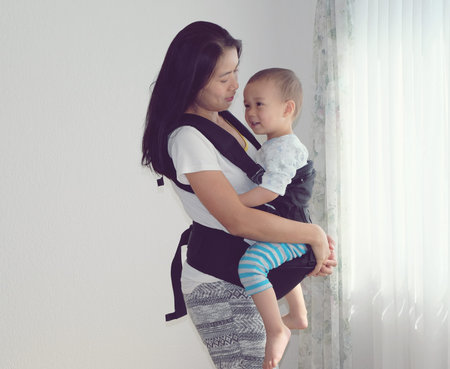 Portrait happy mother carrying her adorable son with baby carrier. Cute boy be happy to be carried...