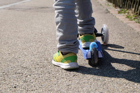Close up of feet riding scooter outdoor. Kid learning to ride scooter.