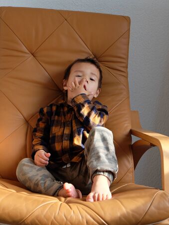 Cheerful little child boy sits happily on rocking chair in bedroom at home.の写真素材