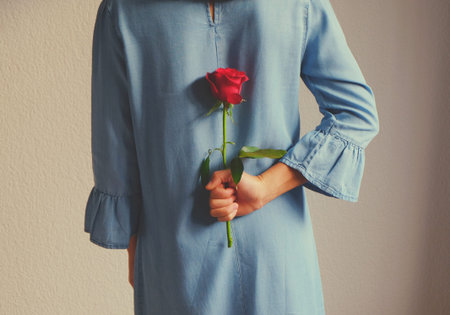 Young Asian lady holding a red rose in hand close up. Love concept idea texture background....