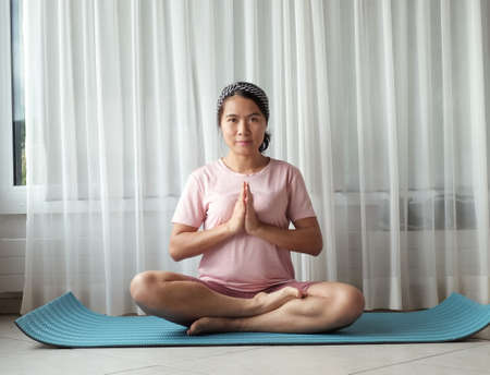 Young Asian woman lady practicing yoga alone in the prayer position at home window light.の写真素材