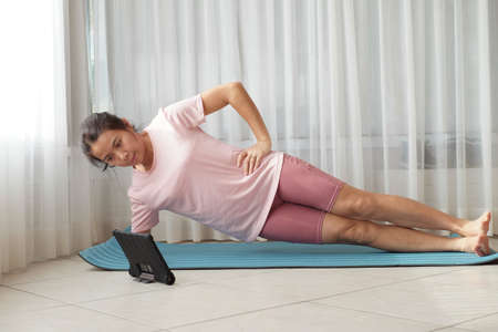Young Asian woman doing class online fitness workout at home window light. New normal Stay home concept idea.の写真素材