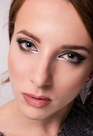Close up beauty portrait of a lovely young grey eyed woman wearing trendy eye makeup looking into the lens with a serious expressionの写真素材