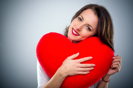 Sentimental young woman in love hugging a large red heart with a tender smile in a Valentines Day conceptの写真素材