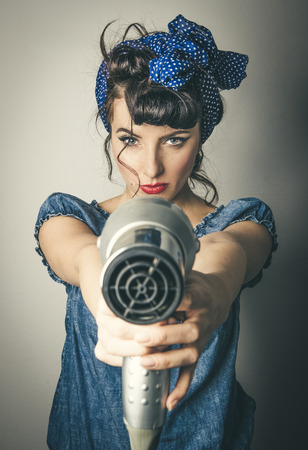 Half body portrait of young woman in vintage clothes pointing hairdryerの写真素材