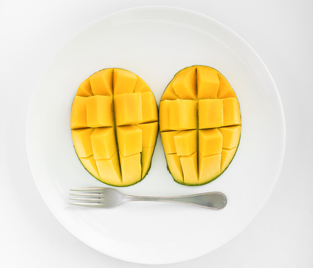 A face made from  two  mangoes and a fork on a white plate with white background.の写真素材