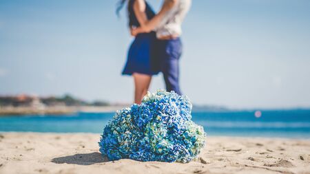 A couple honeymooning at the the beach with a flower bouquet in the foreground.の写真素材
