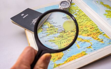 Magnifying glass focused on map of England with passport and watch in the background.の写真素材
