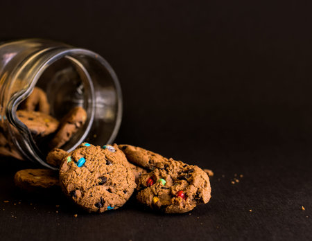 Cookie jar on black background with biscuits spilling out.