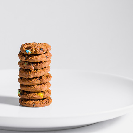 Choc chip  smarties cookies stacked on a white plate.の写真素材