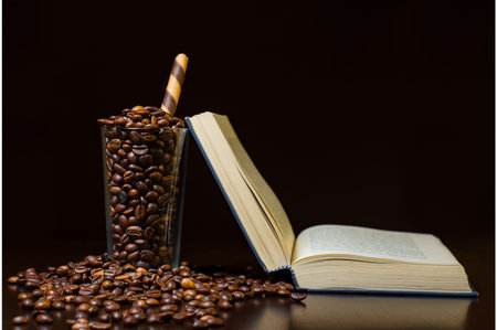 open book on wooden coffee table with coffeee beans in glass and overflowing on tableの写真素材