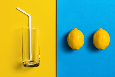 Lemons on split colored background with glass and straw.の写真素材