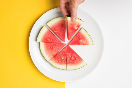 Hand holding slice of watermelon over split color background.の写真素材