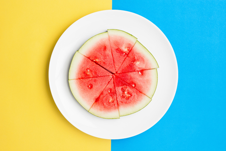 Cut watermelon on round plate with contrasting split color background.の写真素材