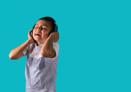 Young boy happily dancing listening to music on headphones  with a blue background and copy space ...