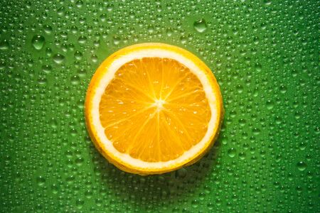 Slice of Orange on green colored background with water droplets creating texture - fresh and healthy food concept imageの写真素材