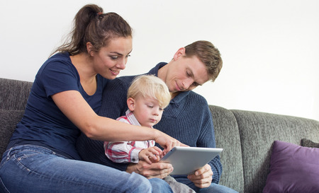 Happy family on couch wit son and tablet pcの写真素材