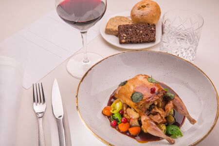 Table layout by the stuffed quail with sauce from a lavender, root crops and red currant with a glass of red wine and a basket of home-made breadの写真素材