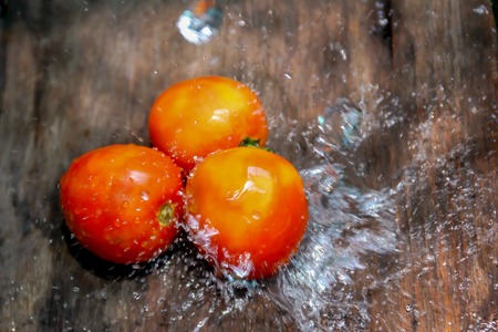 Red Tomato on wooden plate with water splashの写真素材