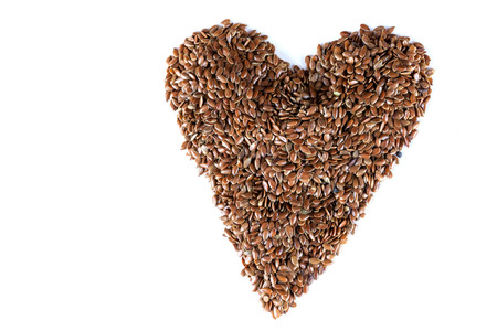a pile of brown flax seeds in heart shape form on isolated white backgroundの写真素材