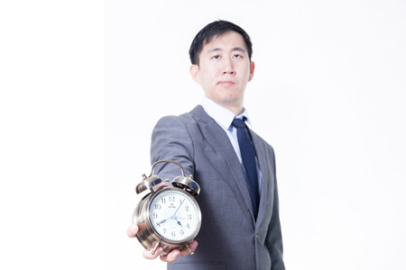 Young Asian businessman holding a clock in unpleasant face expression - business and time conceptの写真素材
