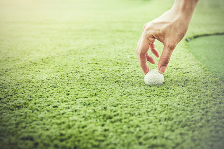 Golfer putting a golf ball onto green grass field - vintage aesthetic toneの写真素材