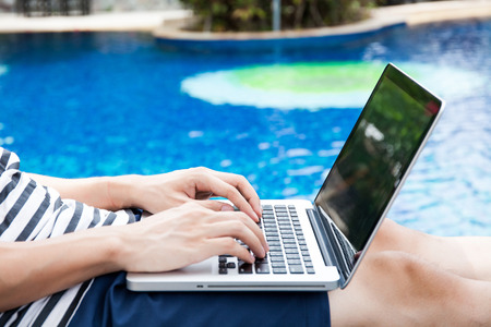 Man using a laptop in the pool on vacation - work anywhere and internet work conceptの写真素材