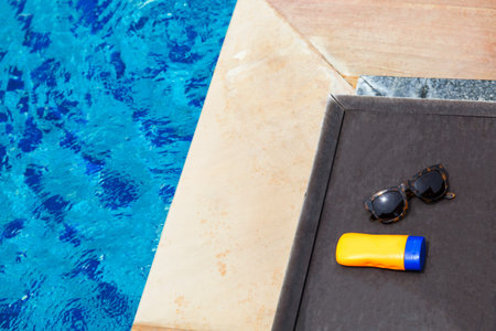Top view of sunglasses and sun lotion on poolside with copy space - summer concept
