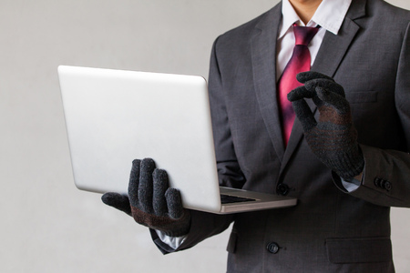 Business man wearing gloves and using computer - fraud, hacker, theft, cyber crime conceptの写真素材