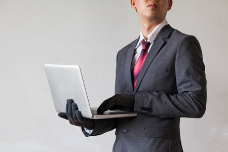 Business man wearing gloves and using computer - fraud, hacker, theft, cyber crime conceptの写真素材