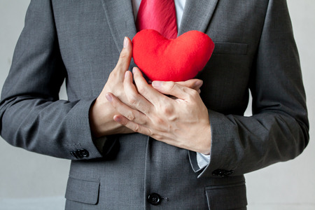Businessman showing compassion holding red heart onto his chest in his suit - crm, service mind business conceptの写真素材