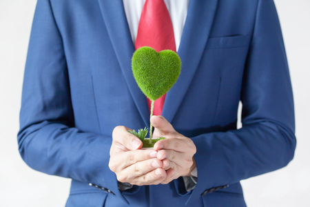 Businessman in suit holding a green heart shape - white background - indicates eco-friendly , social and environmental responsibility business conceptの写真素材