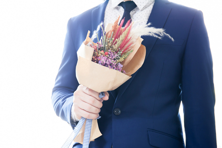 Man in suit holding bouquet with white rim light from background.の写真素材