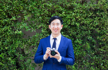 Smiling Asian professional photographer holding vintage camera in green bushes natural backgroundの写真素材