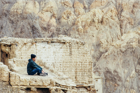 Young male traveler sitting on the sand cliff, thinking about something in Leh, Ladakh, India.の写真素材