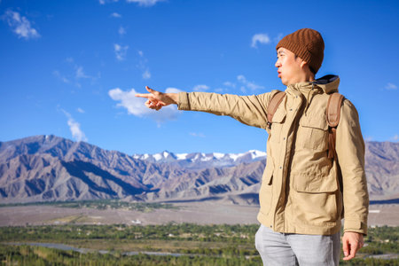 Young Asian traveler pointing out his finger for next destinations in high hill and blue sky background in Leh, Ladakh, Indiaの写真素材