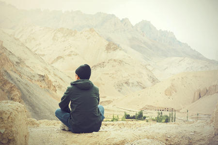Young male traveler sitting on the sand cliff, thinking about something in Leh, Ladakh, India.の写真素材