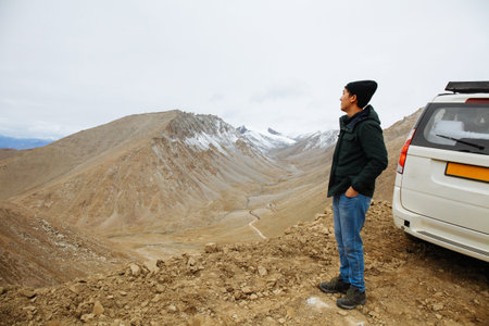 Young and happy man traveler parked car uphill in mountain on roadtrip vacation.の写真素材
