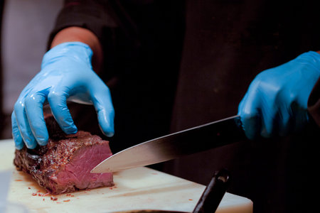 Butcher Cutting Medium Rare Beef on Cutting Board in the Kitchen