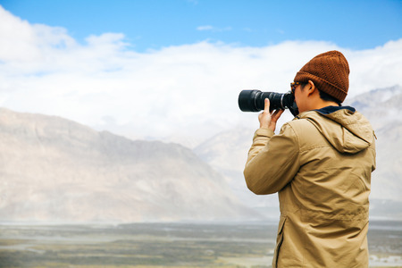 travel photographer journalist holding a dslr camera in mountain background.の写真素材