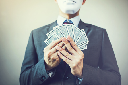 Businessman in mask holding a set of playing cards - hiding expression in business strategic competition concept.の写真素材