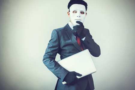 Business man in white mask wearing gloves and stealing computer and digital information - fraud, hacker, theft, cyber crime concept.の写真素材