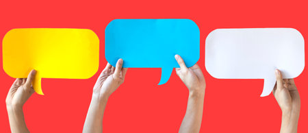 Human Hands Holding Yellow, Blue and White Speech Bubbles Over Light Orange Red Background - Fun...
