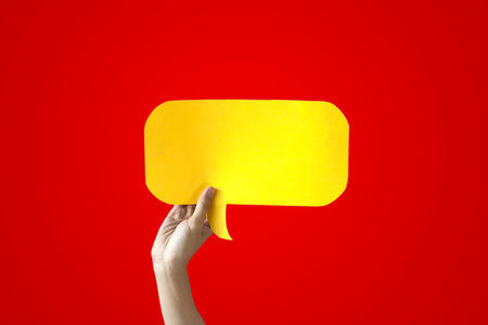 Human Hands Holding Yellow Speech Bubble Over Red Background - Balloon speech bubble conceptの写真素材