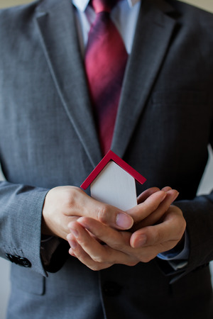Business man in suit having miniature house on palm of his hand - Business mortgage, property loan, house insurance, business investment concept.の写真素材