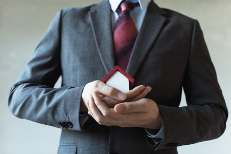 Business man in suit using hands covering and protecting house - Business mortgage, property loan, house insurance, business investment concept.の写真素材